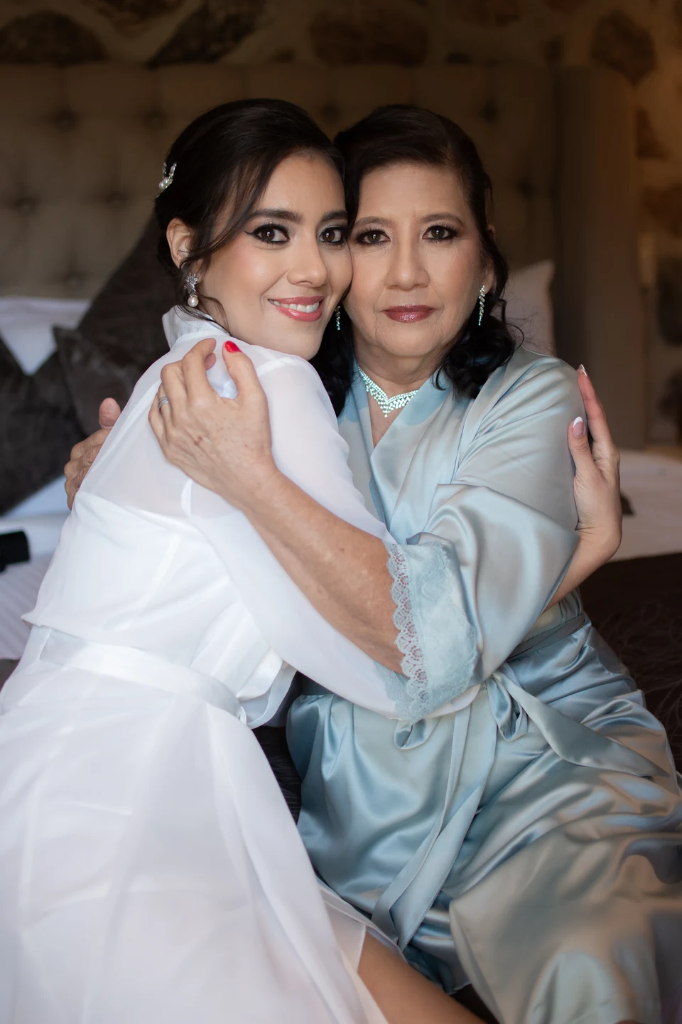 Novia y mama abrazadas, con maquillaje y peinado para la boda.